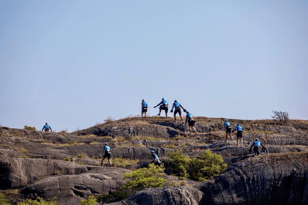 A group of hikers wearing blue shirts navigating rocky terrain under a clear sky.