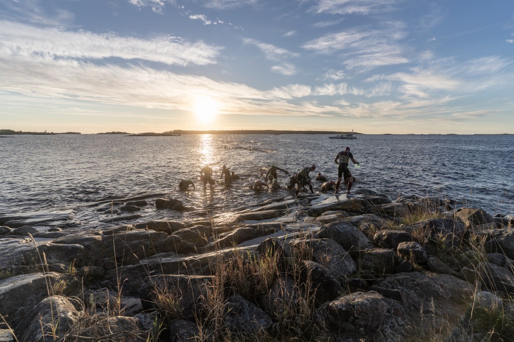 Participants working on rocks by the water's edge at sunset, with a calm sea and distant islands in the background.
